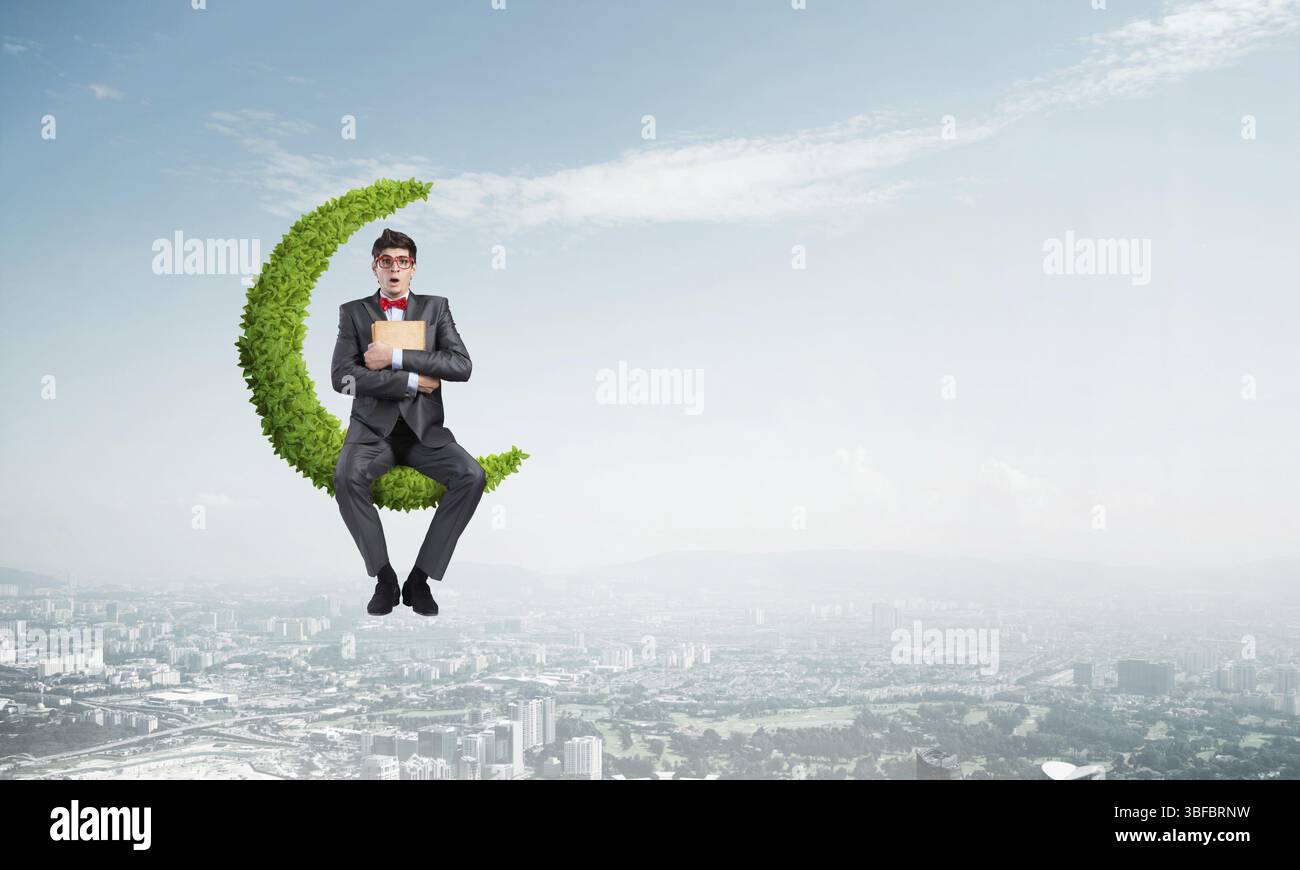 Junger Student mit einem Buch. Sitzt auf dem Symbol des Mondes aus der Pflanze. Vor dem Hintergrund der Stadtlandschaft Stockfoto