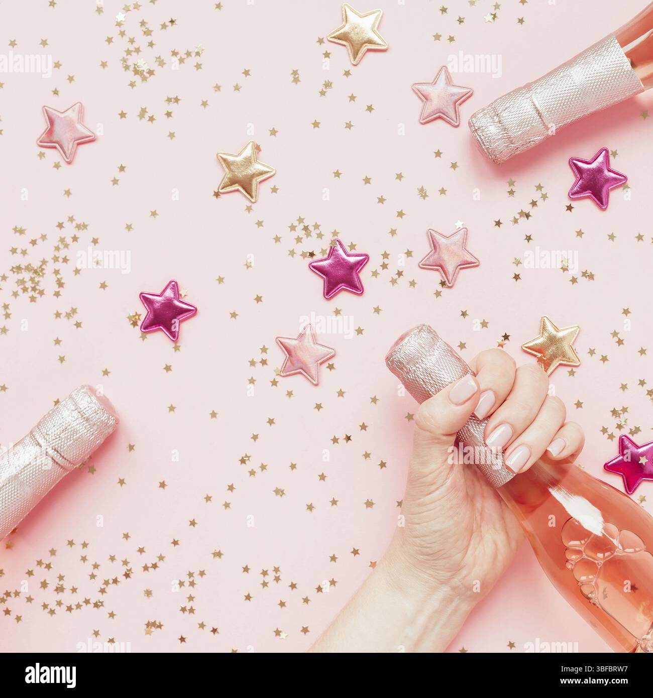 Weihnachten oder Neujahr Zusammensetzung mit Flasche Rose Champagne in der Frau die Hand und golden glänzenden funkeln Sterne Konfetti auf Pastell rosa Hintergrund, oben vi. Stockfoto