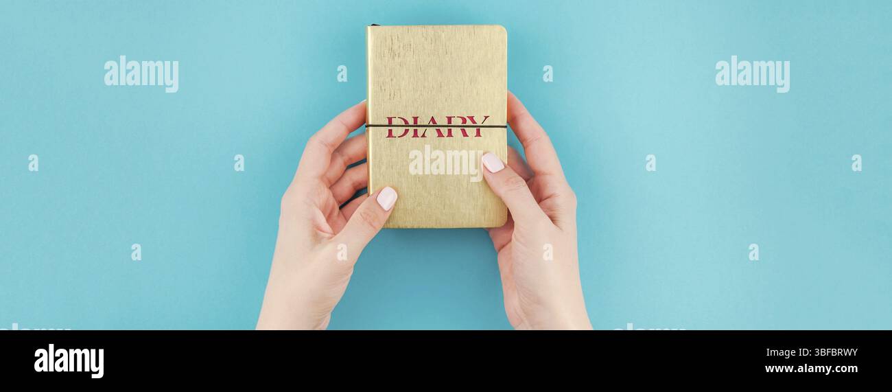 Lange breite Fahne von Frau Hände, die kleine goldene Notizbuch Tagebuch mit Kopie Speicherplatz auf Türkis Papier Hintergrund in minimalistischem Stil. Vorlage für Fe Stockfoto