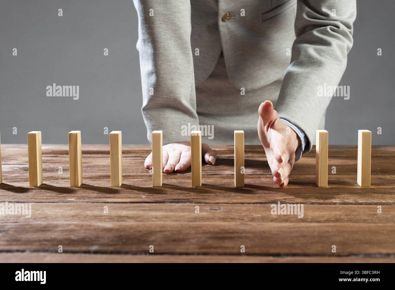 Geschäftsfrau unterbricht Domino-Effekt, indem sie aufhört, hölzerne Dominosteine zu fallen. Operative Geschäftslösung, Strategie und erfolgreiche Intervention. Unternehmen Stockfoto