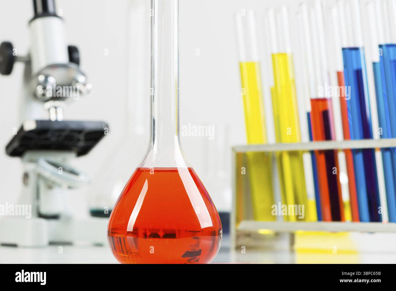 Schulchemielabor mit Glaswaren und Mikroskop. Reagenzgläser und -Kolben mit Farbflüssigkeit stehen auf dem Schreibtisch. Schulbildung und Mikrobiologie Stockfoto