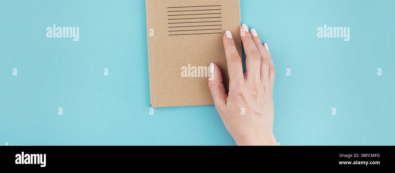 Lange breite Fahne von Frau Hände halten Handwerk Notizbuch aus Papier Tagebuch mit Kopie Speicherplatz auf Türkisfarbenem Hintergrund in minimalistischem Stil. Vorlage für feminine Stockfoto