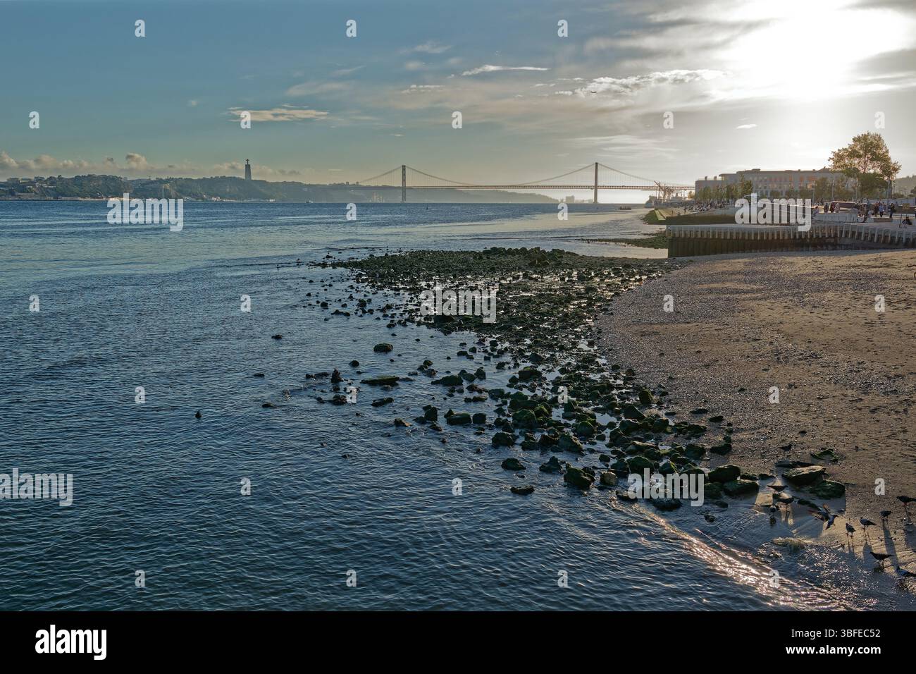 Eine Luftaufnahme zeigt einen Blick auf den Tejo in Lissabon, Portugal. Der Vordergrund zeigt einen schwarzen Sandstrand mit zahlreichen kleinen Felsen und Kieselstein Stockfoto
