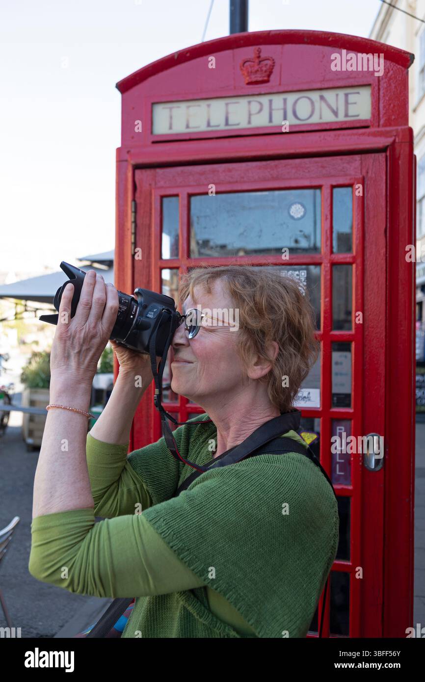 Ältere Frau, die Fotos mit Spiegelreflexkamera macht, rote Telefonzelle, Oxford, England, Großbritannien Stockfoto