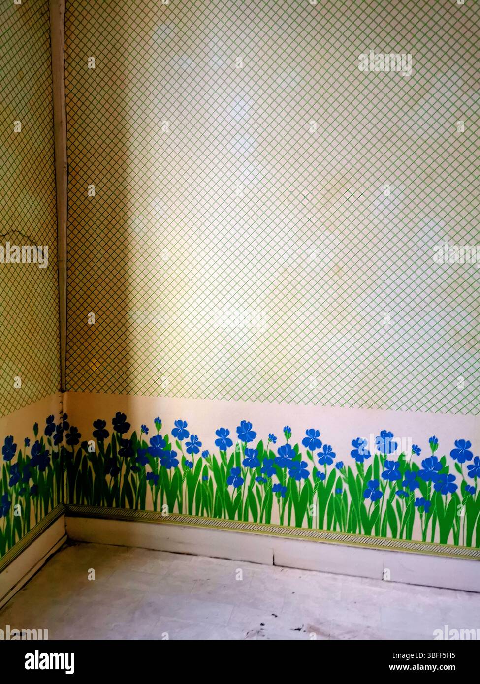 Ein leeres Eckzimmer verfügt über ein einzigartiges Wanddesign mit leuchtenden blauen Blumen und grünem Gras, das entlang der Basis bemalt ist. - Smartphone-aufgenommenes Stockfoto