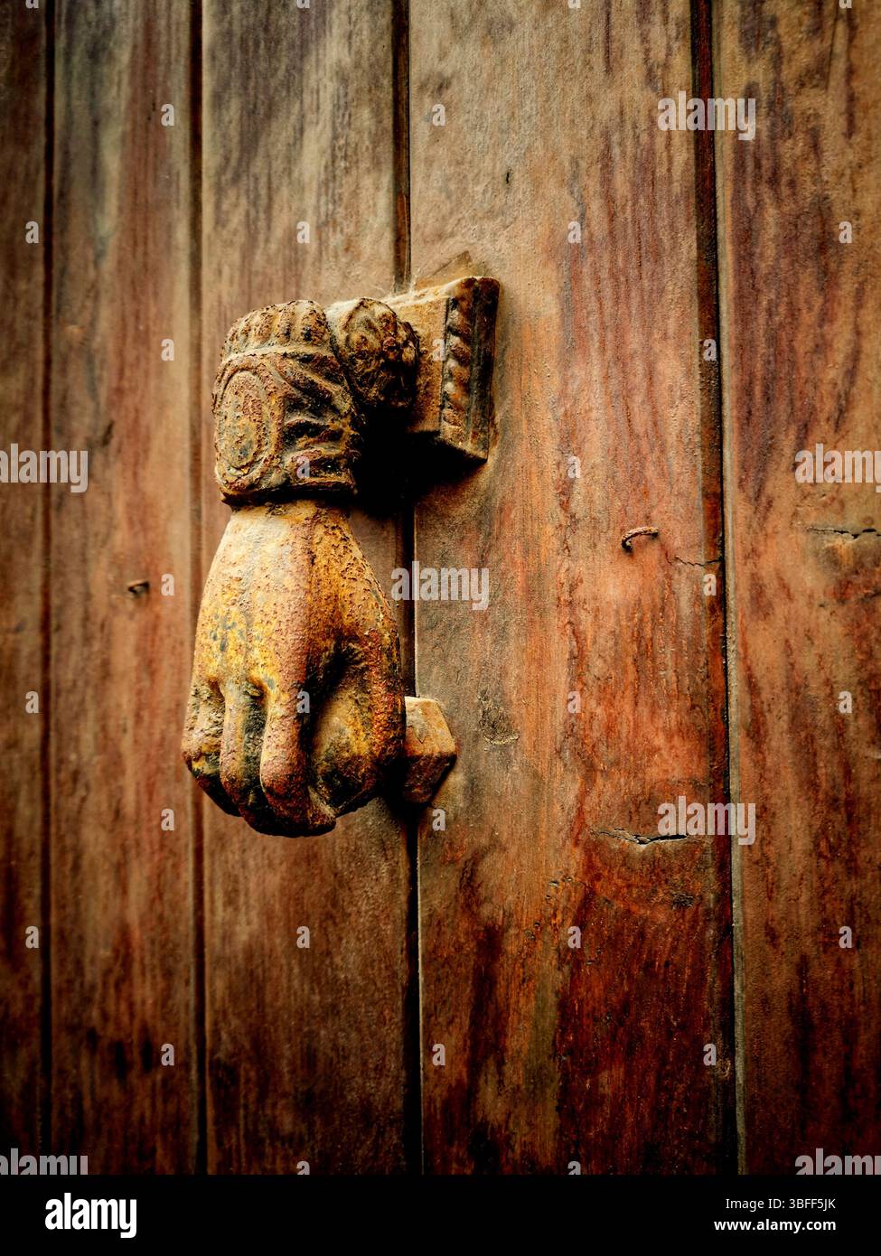 Auf einer verwitterten Holztür befindet sich ein handgeformter Türklopfer im Vintage-Stil, der komplexe Designs und eine satte Patina präsentiert Stockfoto