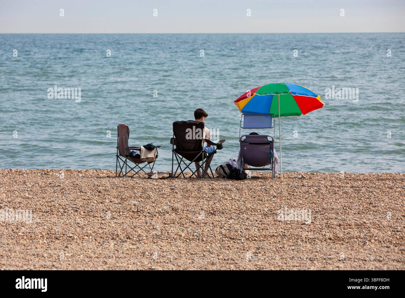 Eine kleine Familiengruppe, die an einem Kieselstrand am ruhigen blauen Meer Urlaub macht Stockfoto