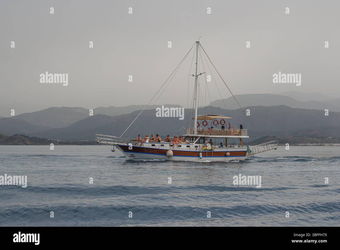 Genießen Sie eine herrliche Tagestour auf einem klassischen türkischen Boot in Fethiye. Die Menschen sind auf dem oberen Deck zu sehen und genießen die wunderschöne Aussicht auf die Küste. Stockfoto