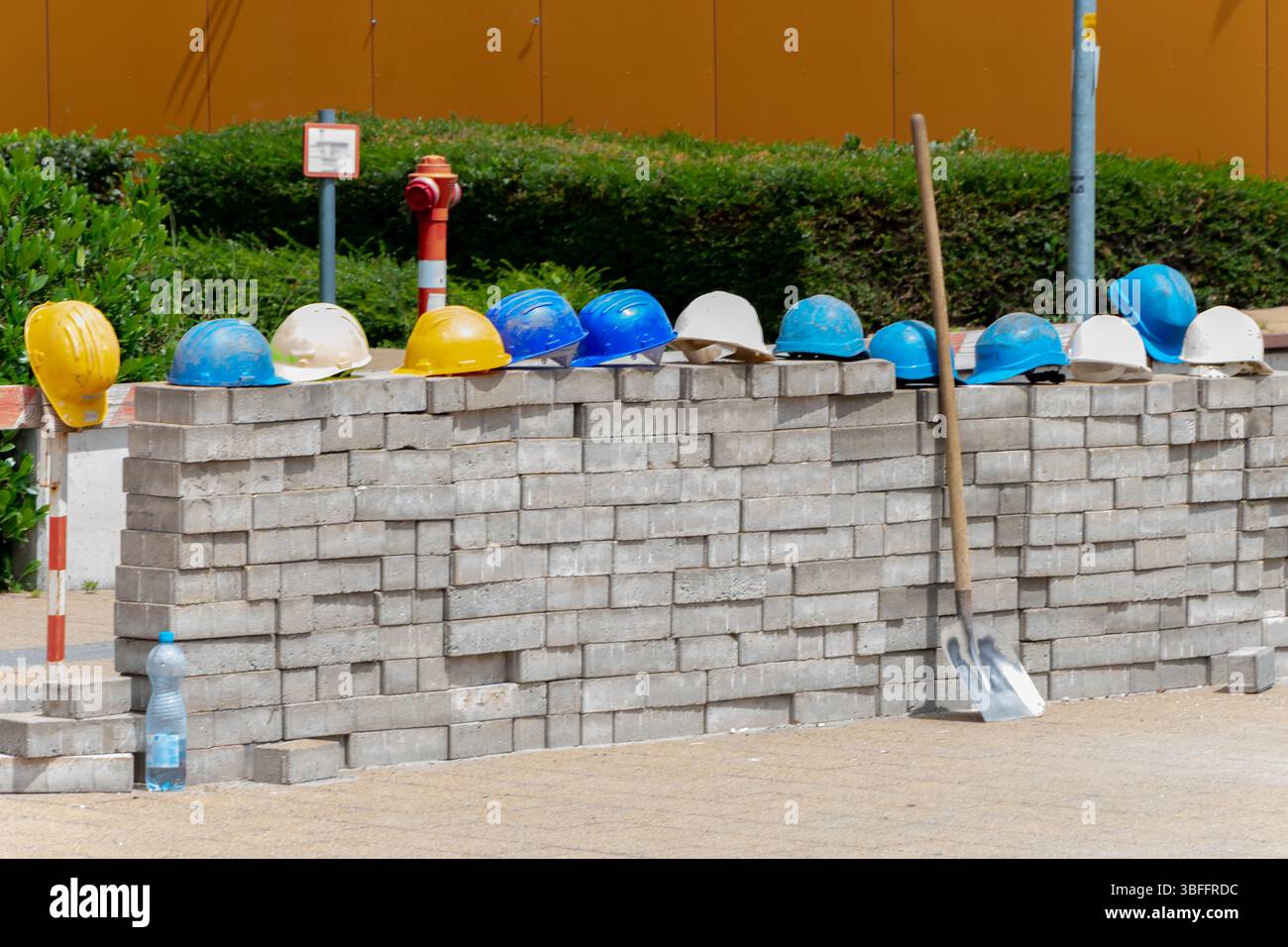 Baustellenhelme: Mehrfarbige Bauhelme, die ordentlich auf einer Ziegelwand gestapelt sind, symbolisieren Sicherheit und Arbeitsabläufe auf einer Baustelle Stockfoto