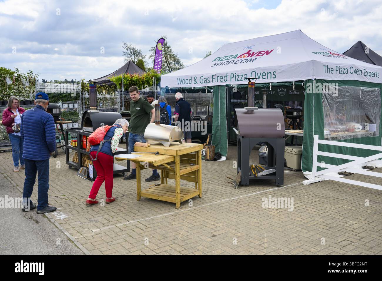 Ausstellungsstand für Pizzaöfen, Besucher im Internet und Verkäufer im Ausstellungsraum - Harrogate Spring Flower Show 2025, Yorkshire England, Großbritannien. Stockfoto