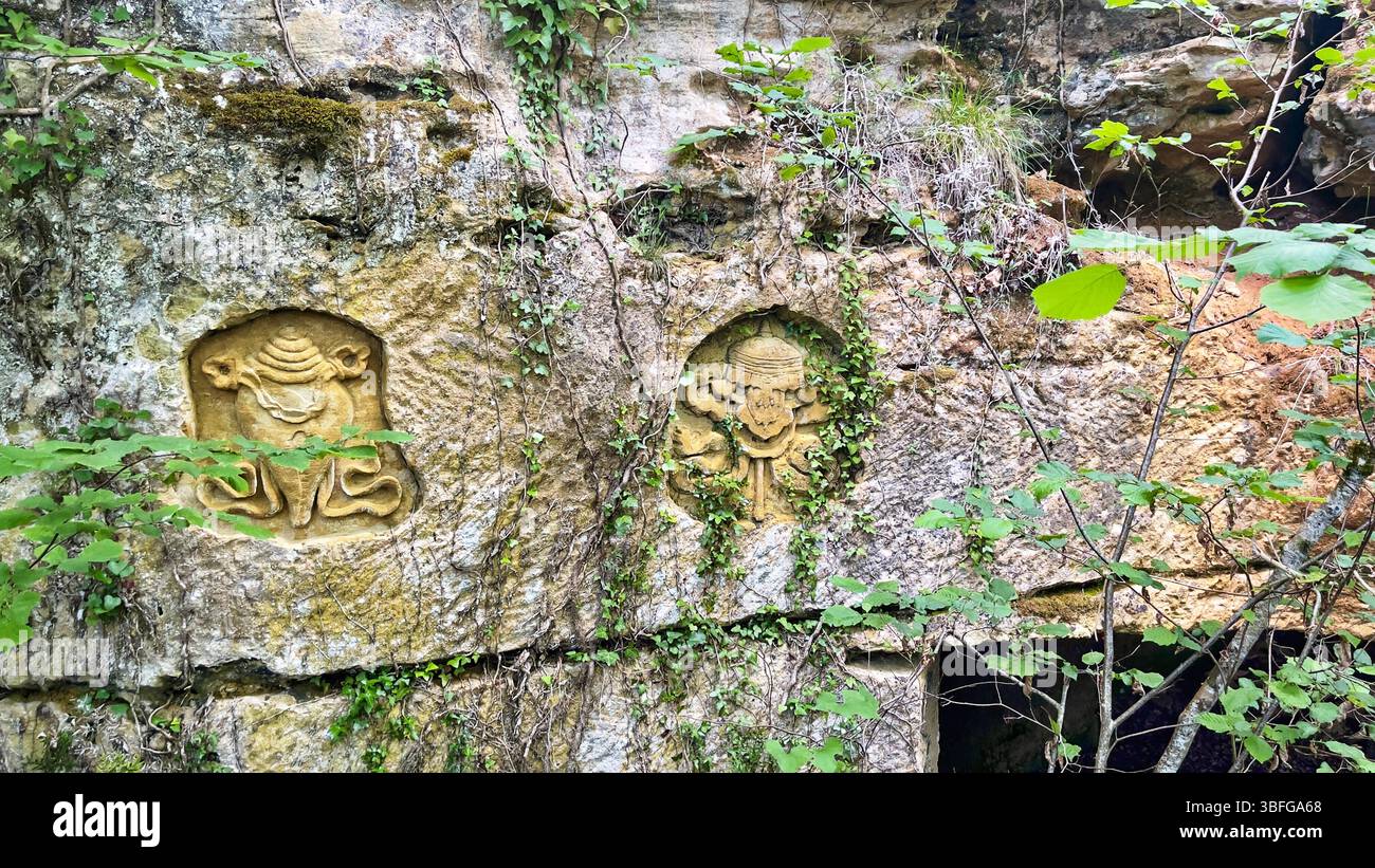 Aus dem Stein ragen aufwendig geschnitzte buddhistische Figuren hervor, die spirituelle Hingabe und künstlerisches Erbe in der Nähe von Saint-Léon-sur-Vézère, Frankreich, verkörpern Stockfoto