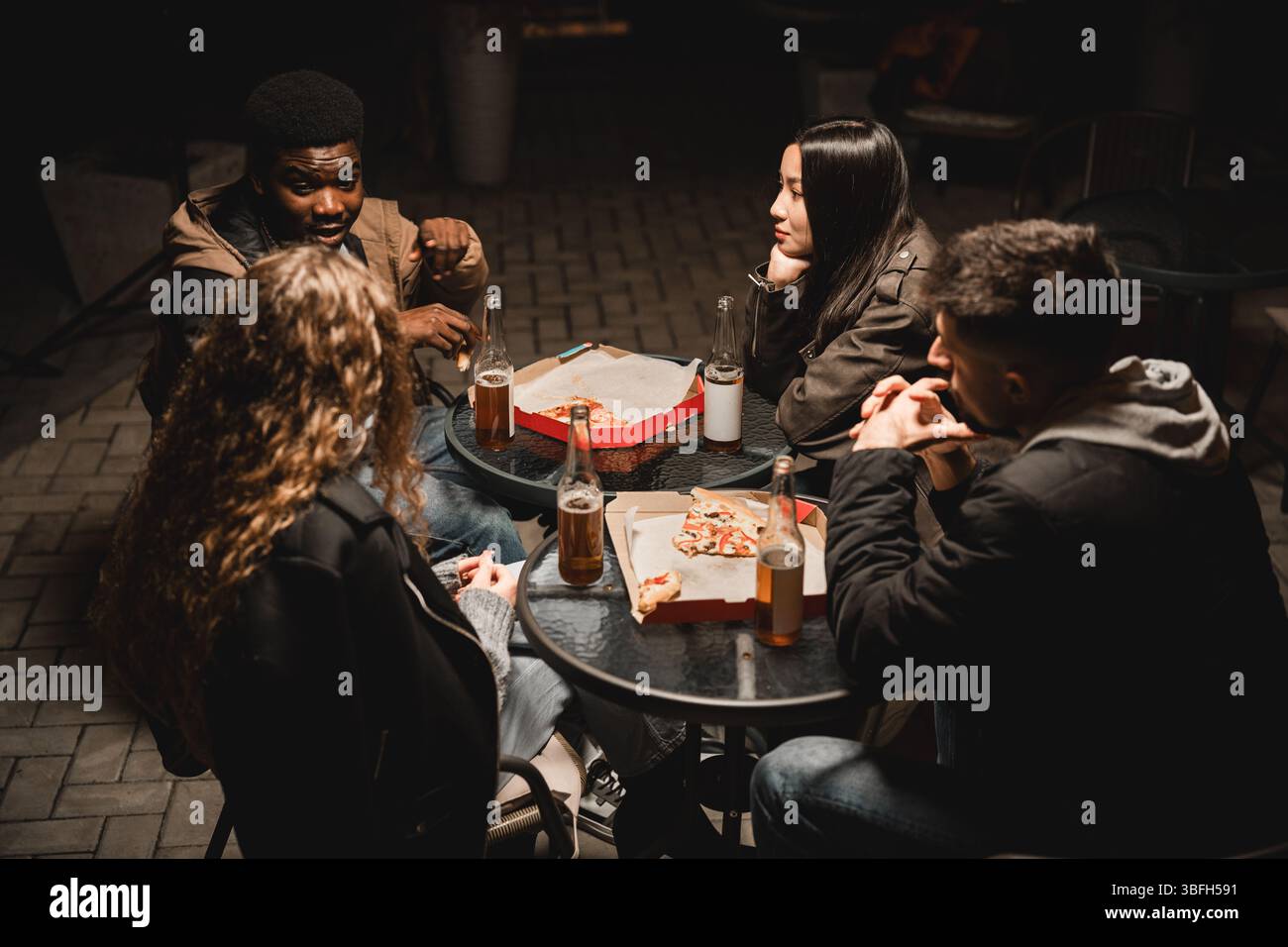 Eine Gruppe von Freunden genießt nachts Pizza und Getränke im Freien in gemütlicher Atmosphäre Stockfoto