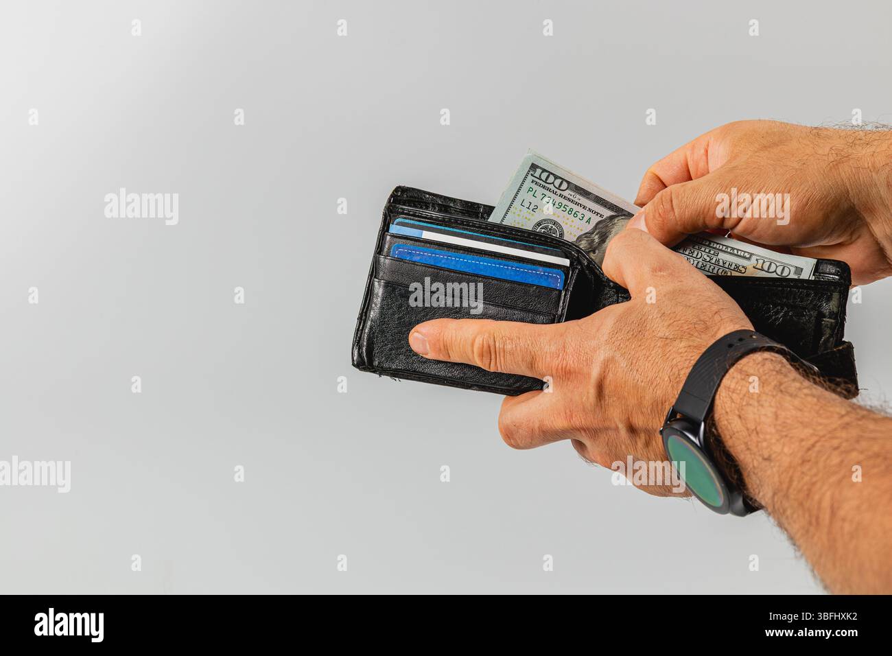 Eine Person hält eine schwarze Brieftasche und holt mehrere Banknoten ab, während Karten sichtbar sind. Die Hände sind stabil und konzentrieren sich darauf, Bargeld und Karten sorgsam zu verwalten Stockfoto