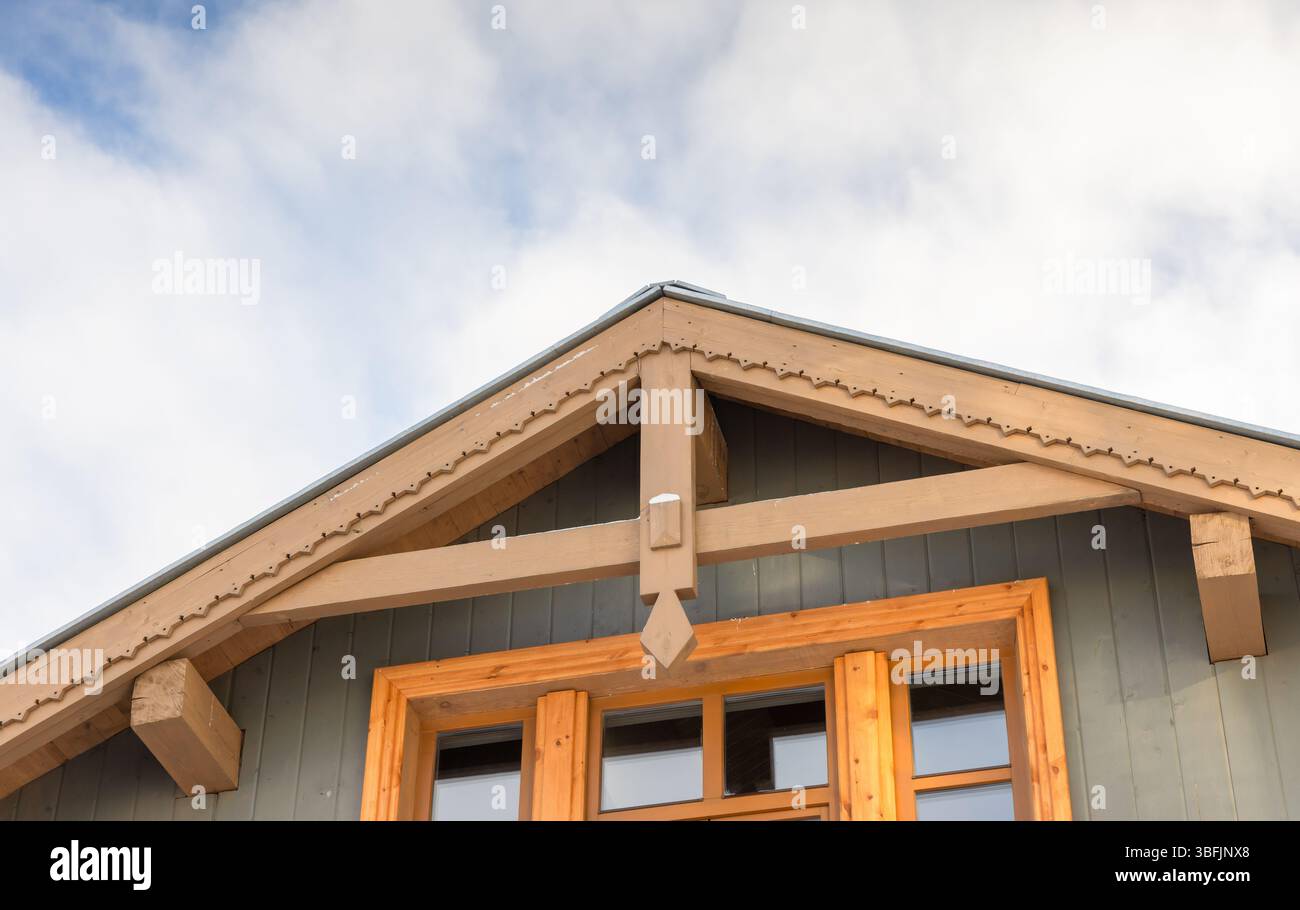 Architektonisches Detail eines Hausdachs mit Holzkonstruktion mit blauen Wänden und hellen Highlights unter einem verstreuten Wolkenhimmel Stockfoto