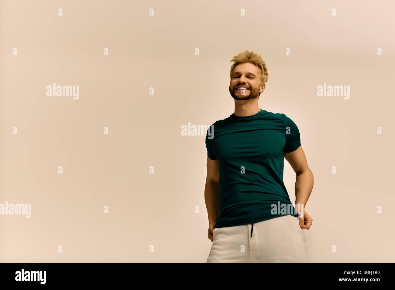 Hübscher junger Mann, der fröhlich lächelt, während er sich in einer einfachen Innenumgebung entspannt. Stockfoto