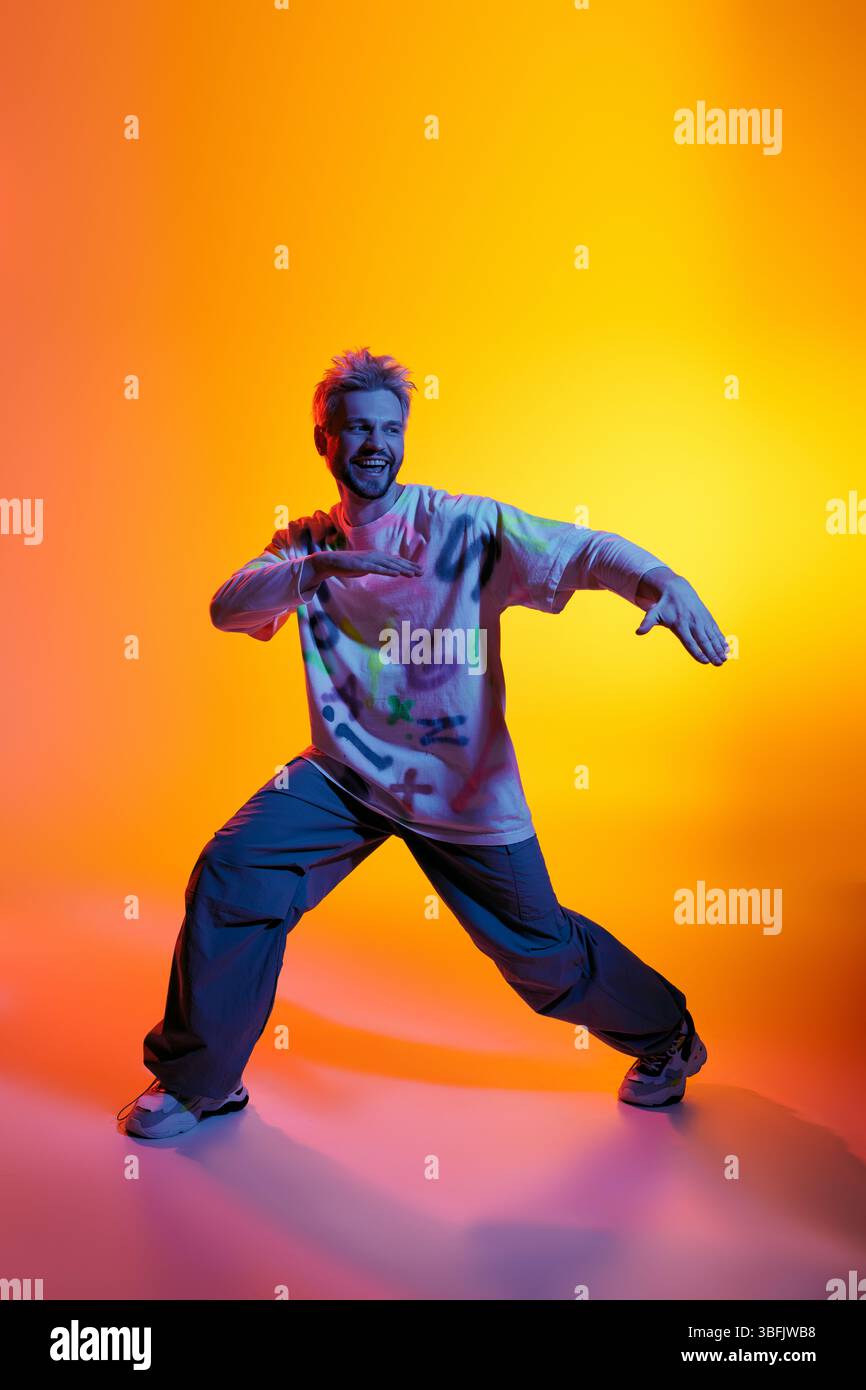Lebhafter junger Mann, der energiegeladene Tanzbewegungen inmitten farbenfroher Lichter vorführt. Stockfoto