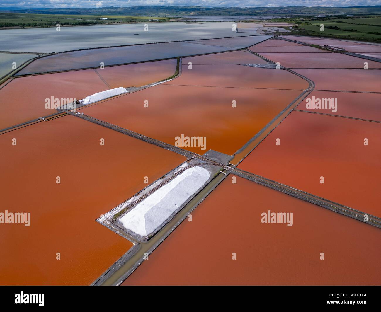 Aus der Vogelperspektive der farbenfrohen Salinen in der Nähe von Burgas, Bulgarien. Leuchtend rote und orangene Verdunstungsteiche stehen im Kontrast zu weißen Salzhaufen und türkisfarbenem Meer Stockfoto