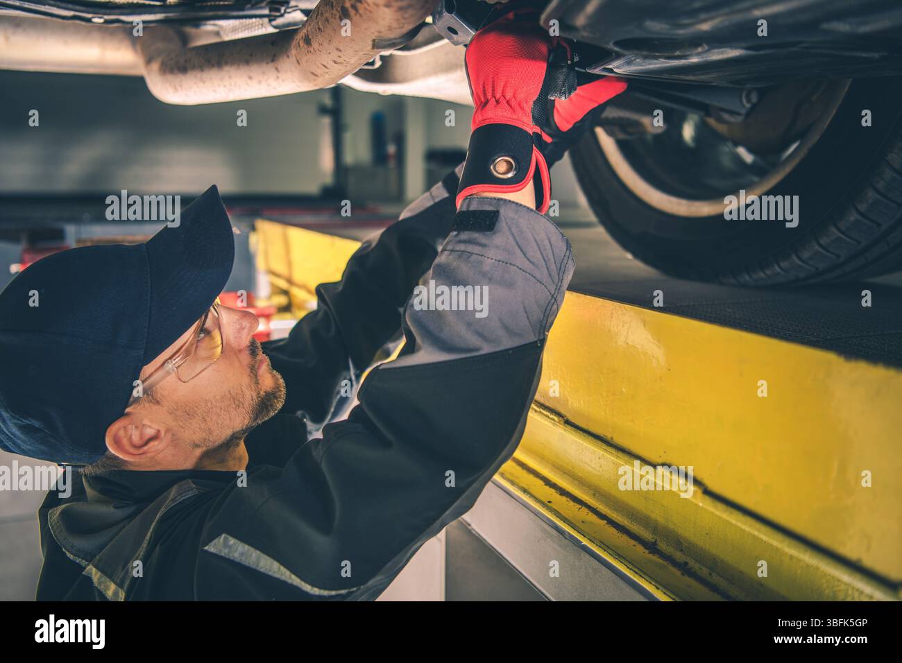 Ein erfahrener Mechaniker arbeitet in einer hellen Werkstatt am Laufwerk eines Fahrzeugs, um die optimale Leistung und Sicherheit des Fahrzeugs zu gewährleisten. Stockfoto