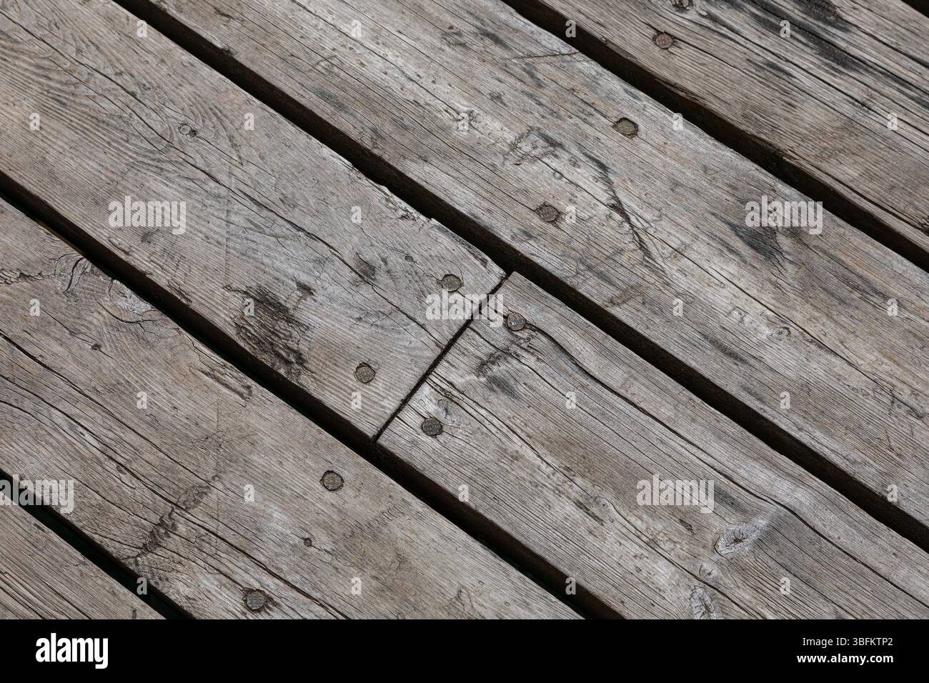 Nahaufnahme diagonaler Holzdielen mit sichtbarer Körnung und Nägeln. Verwitterte Oberflächenstruktur, ideal als rustikaler Hintergrund oder Designelement. Stockfoto
