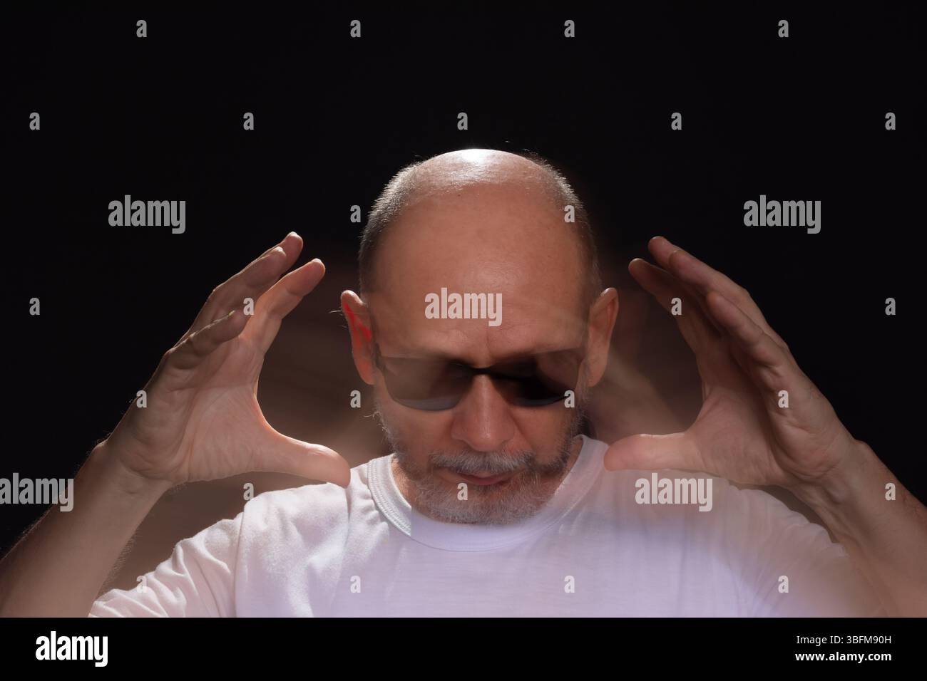Künstlerisches Porträt eines bärtigen Glatzen-Mannes in weißem Hemd, der Bewegungen mit Armen und Händen verwischt. Schwarzer Hintergrund. Stockfoto