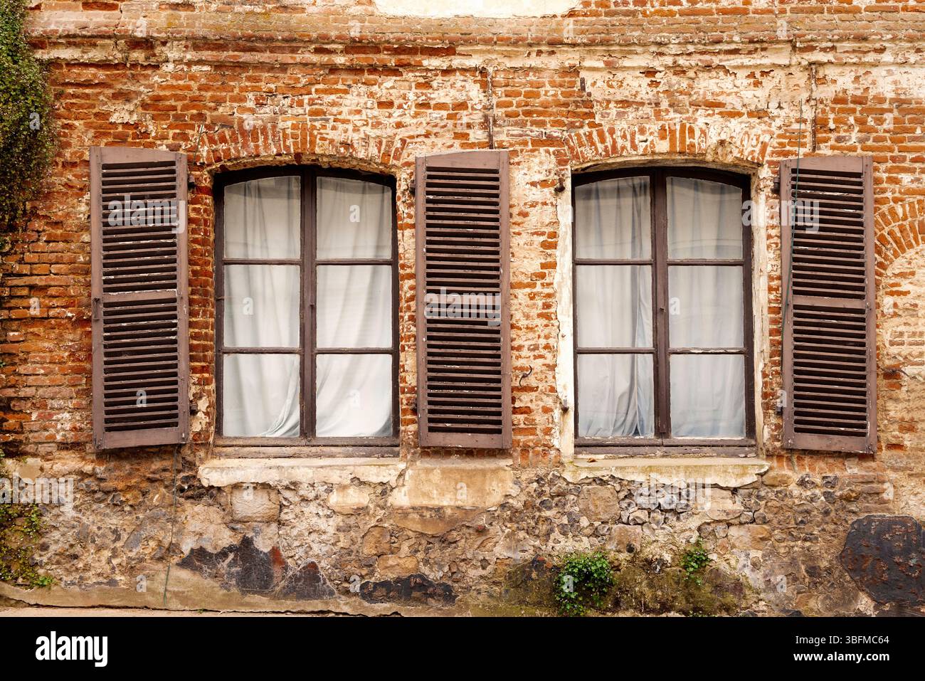 Zwei Fensterrahmen mit klapprigen Fensterläden in einem alten französischen Backsteingebäude. Frankreich. Stockfoto