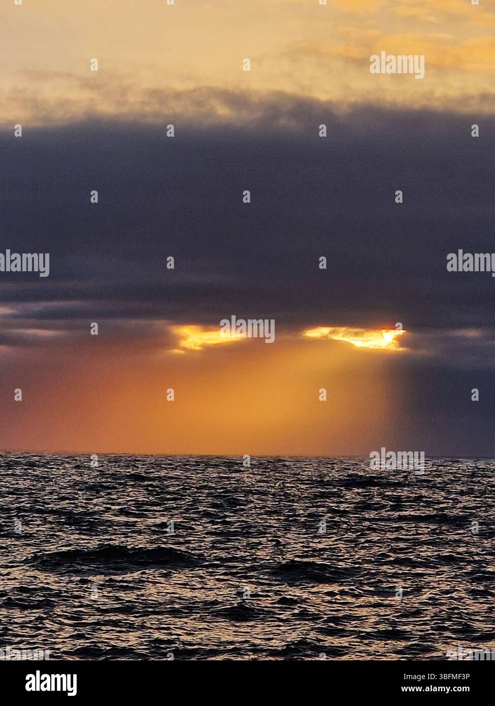 Dramatische „Augen“ bei Sonnenuntergang über dem Ozean mit leuchtenden Farben und bewölktem Himmel. Brighton, Großbritannien Stockfoto