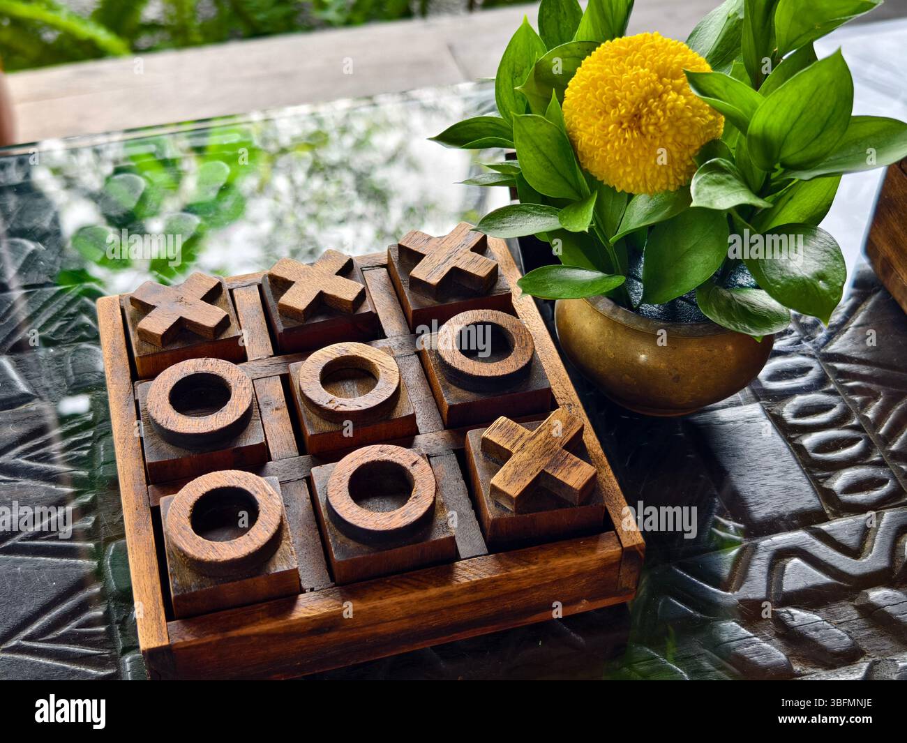 Ein handgefertigtes Holz-Tic-Tac-Toe-Brett und eine Messingblumenvase Stockfoto