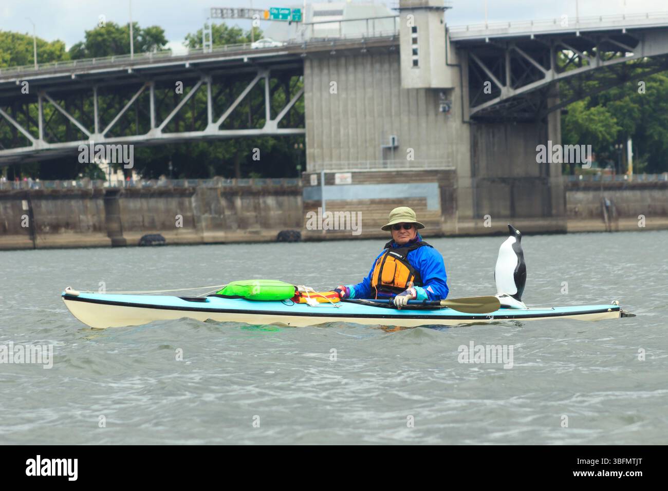 The Big Float, Portland, Oregon – 10. Juli 2016: Ein Kajakfahrer paddelt auf dem Willamette River mit einer Pinguinstatue auf der Rückseite des Bootes. Stockfoto