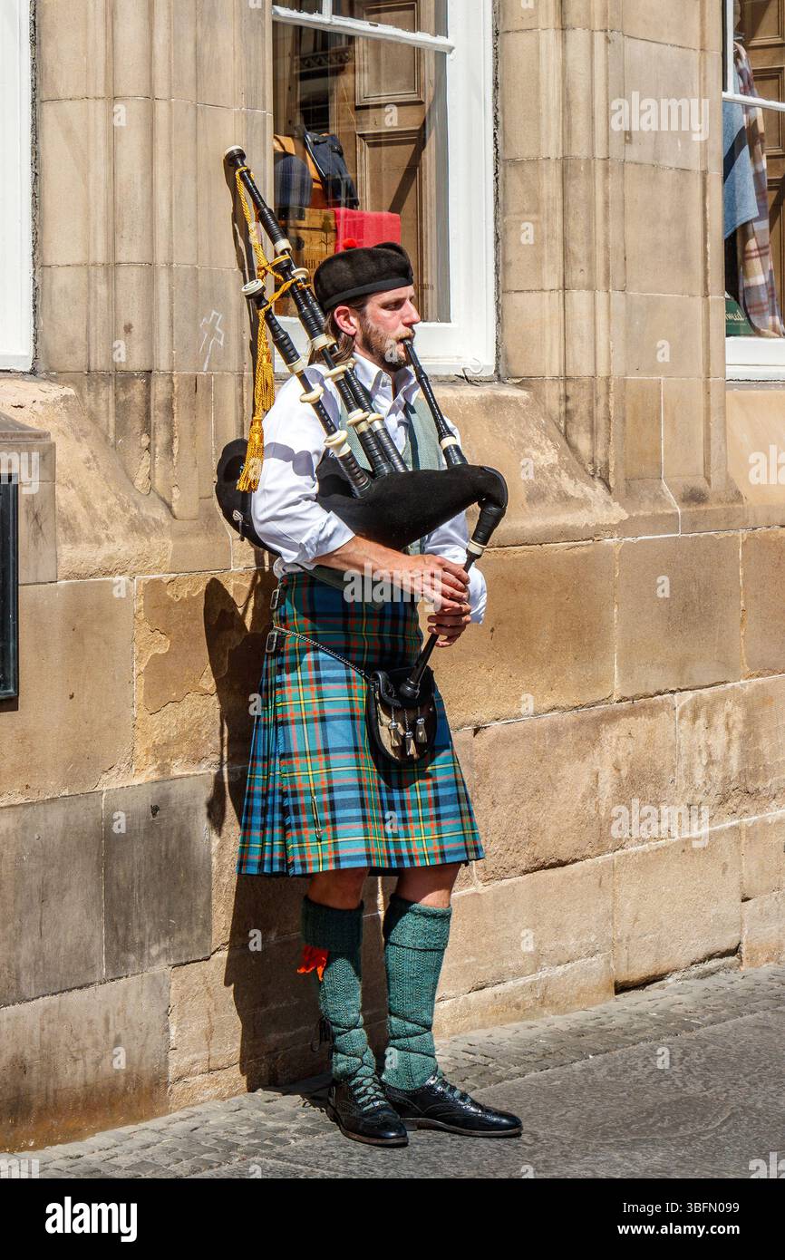 Ein Mann in traditioneller schottischer Kleidung spielt an einem sonnigen Tag in edinburgh schottland den Dudelsack vor einem historischen schottischen Steingebäude Stockfoto