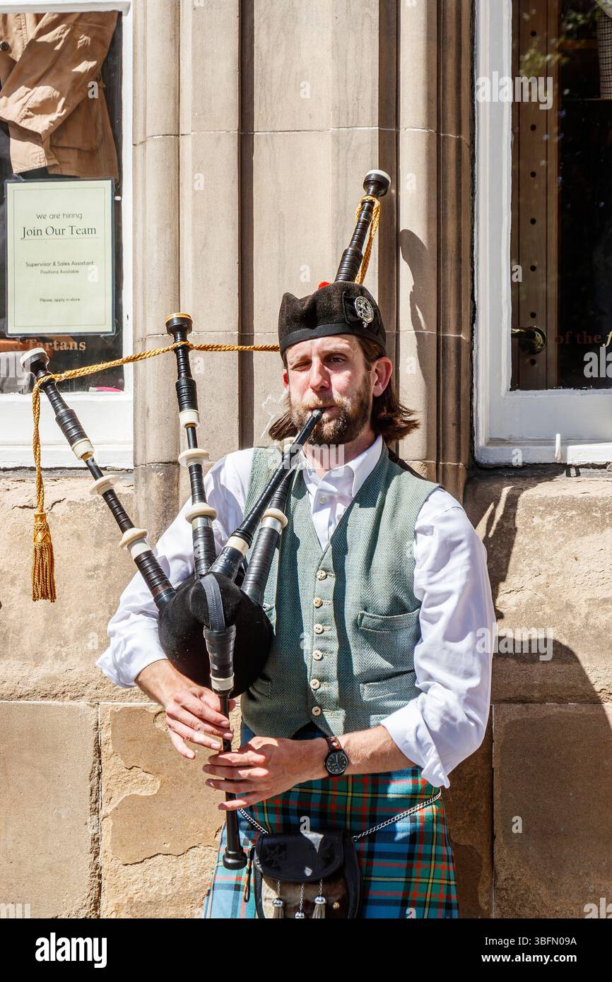 Ein Mann in traditioneller schottischer Kleidung spielt an einem sonnigen Tag in edinburgh schottland den Dudelsack vor einem historischen schottischen Steingebäude Stockfoto