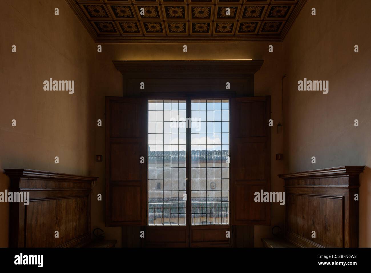 Innenansicht eines sonnendurchfluteten Zimmers mit großem Holzfenster, geschnitzten Bänken und Kassettendecke, zweiter Stock des San Marco Klosters, Florenz, Italien. Stockfoto Innenansicht eines sonnendurchfluteten Zimmers mit großem Holzfenster, geschnitzten Bänken und Kassettendecke, zweiter Stock des San Marco Klosters, Florenz, Italien. Stockfoto