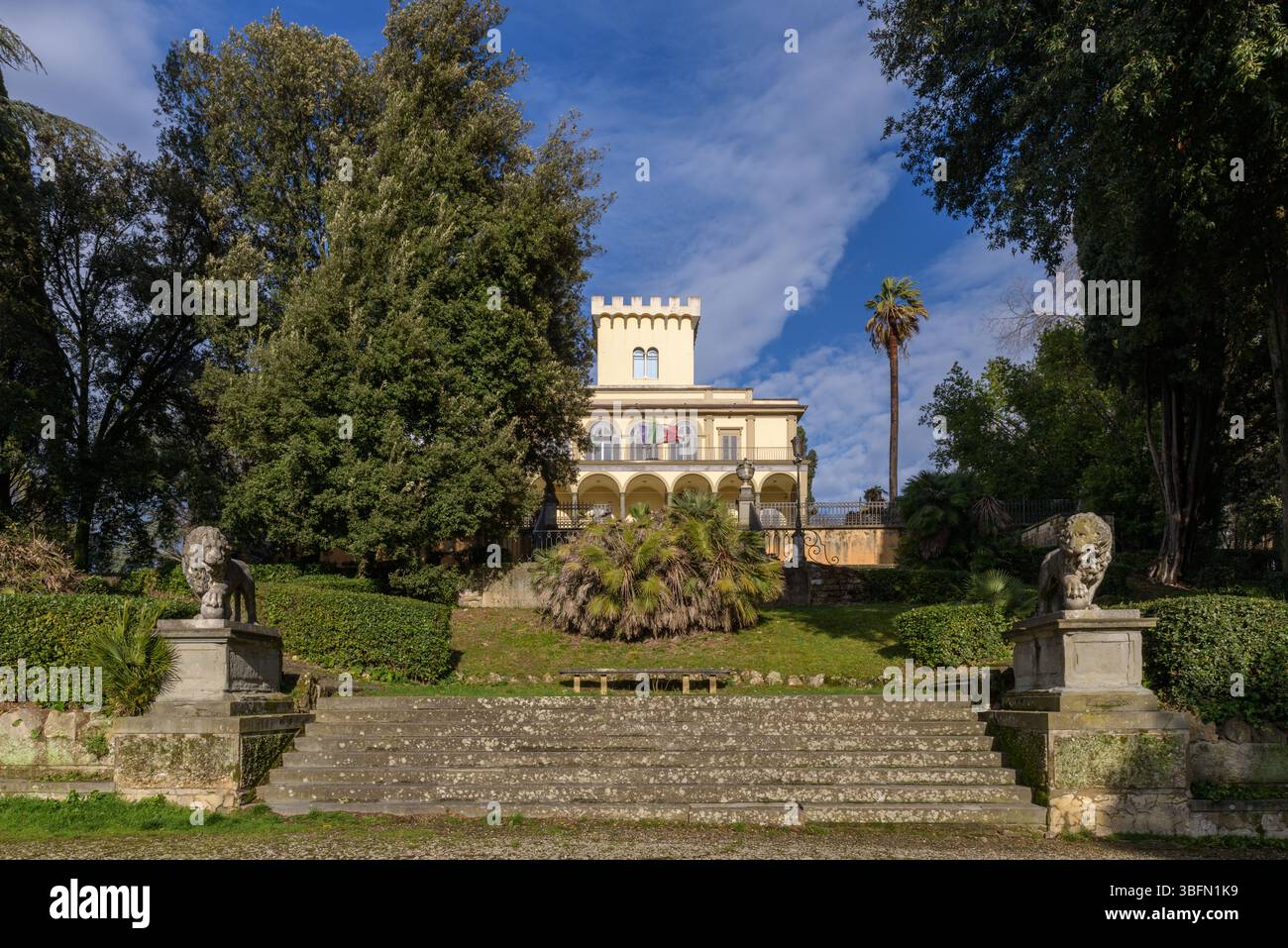 Blick auf die Villa Fabbricotti in Florenz mit zinnenförmigem Turm, Bogenloggia, Gartentreppe und Löwenstatuen unter blauem Himmel. Stockfoto