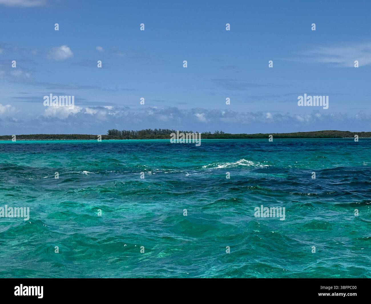 Lebendiges türkisfarbenes Meer mit einer entfernten tropischen Insel unter einem klaren blauen Himmel. Stockfoto