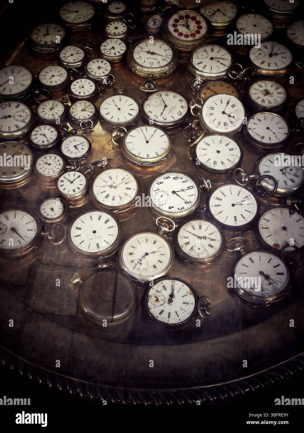 In einem Antiquitätengeschäft sind verschiedene Vintage-Taschenuhren ordentlich auf einer reflektierenden Oberfläche angeordnet Stockfoto