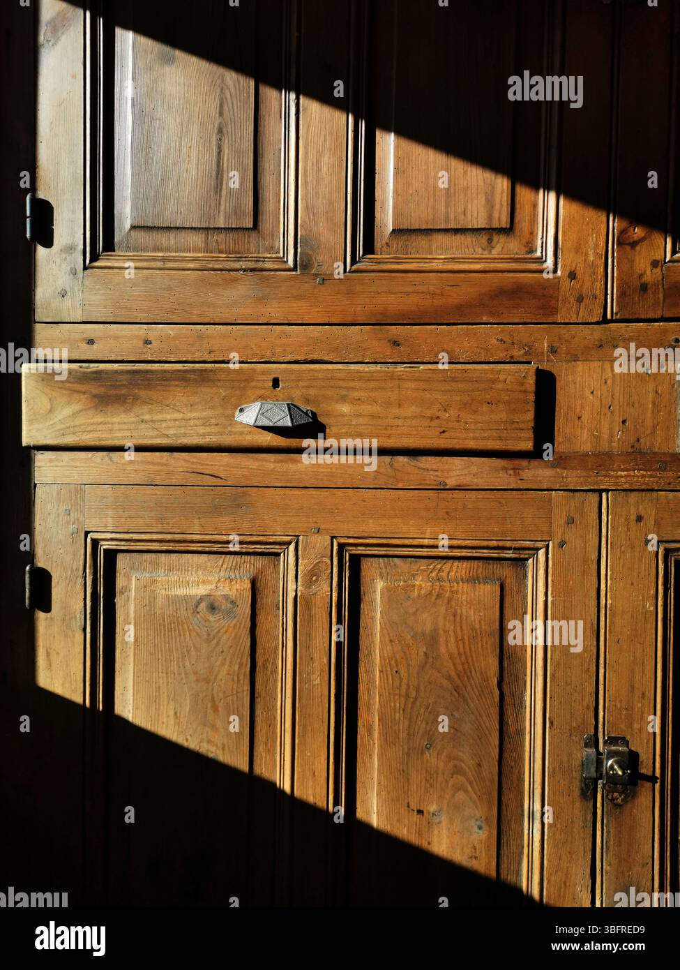 Ein Vintage-Holzschrank verfügt über eine markante Schublade, die in warmes Sonnenlicht getaucht ist und Schatten wirft. - Smartphone-aufgenommenes Stockfoto