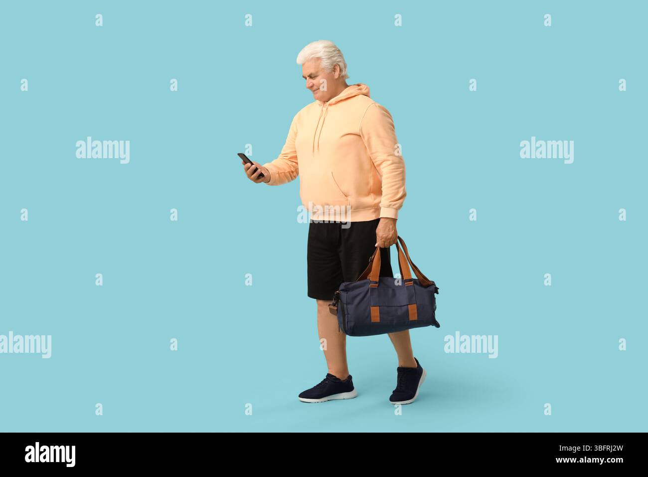 Seniorenmann mit Sporttasche mit Handy auf blauem Hintergrund Stockfoto