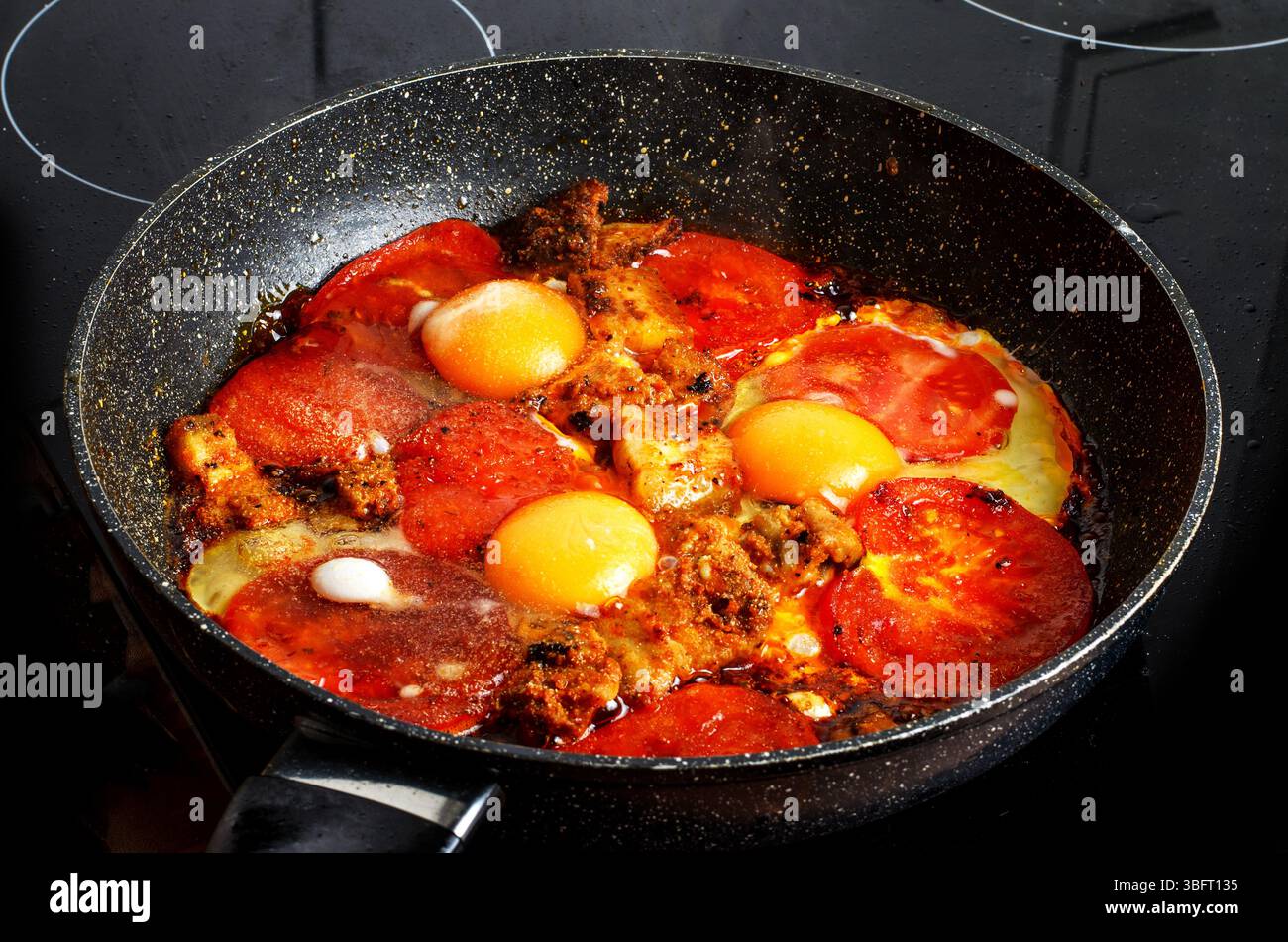 Spiegeleier mit Speck und Tomaten in einer Pfanne auf dem Herd Stockfoto