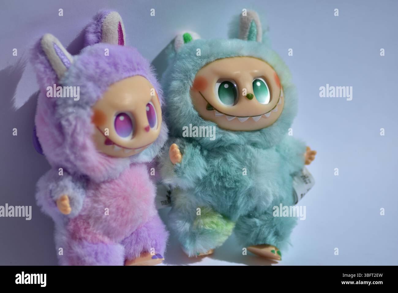Zwei verspielte Labubu-Spielzeugfiguren in flauschigen blau-rosa Monsterkostümen und einem schelmischen Lächeln vor weißem Hintergrund. Stockfoto