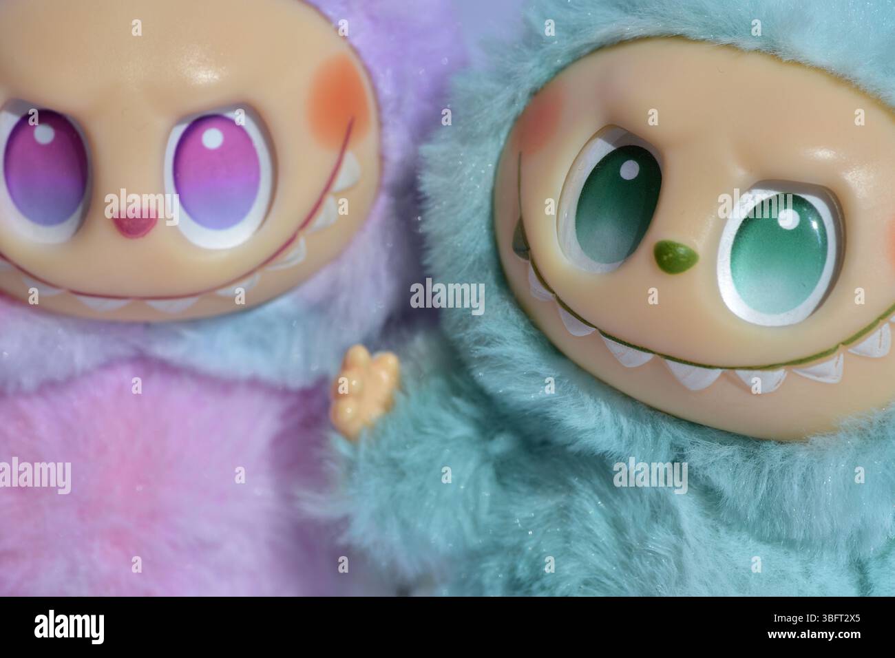Zwei verspielte Labubu-Spielzeugfiguren in flauschigen blau-rosa Monsterkostümen und einem schelmischen Lächeln vor weißem Hintergrund. Stockfoto