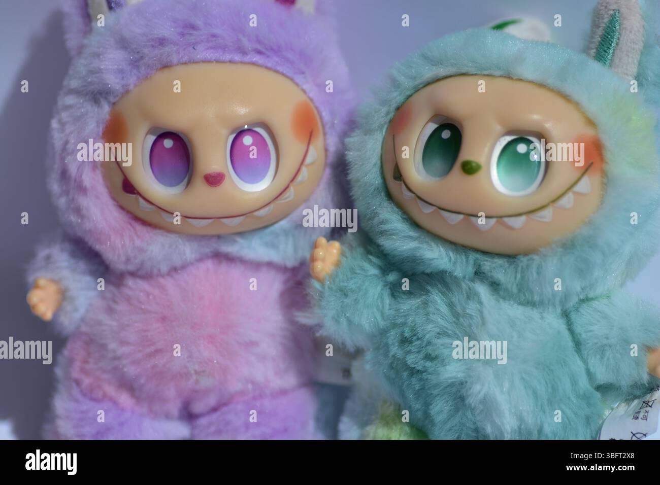 Zwei verspielte Labubu-Spielzeugfiguren in flauschigen blau-rosa Monsterkostümen und einem schelmischen Lächeln vor weißem Hintergrund. Stockfoto