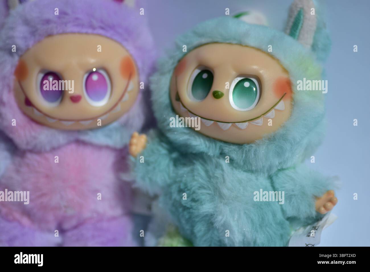 Zwei verspielte Labubu-Spielzeugfiguren in flauschigen blau-rosa Monsterkostümen und einem schelmischen Lächeln vor weißem Hintergrund. Stockfoto