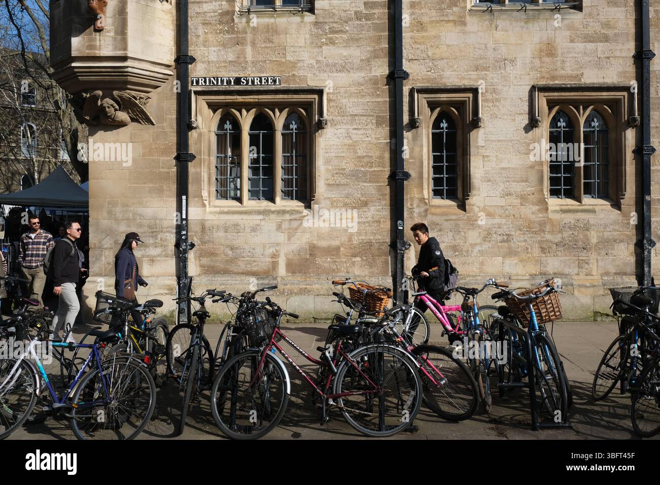 An einem sonnigen Tag laufen die Leute an geparkten Fahrrädern auf der Trinity Street im Zentrum von Cambridge vorbei Stockfoto