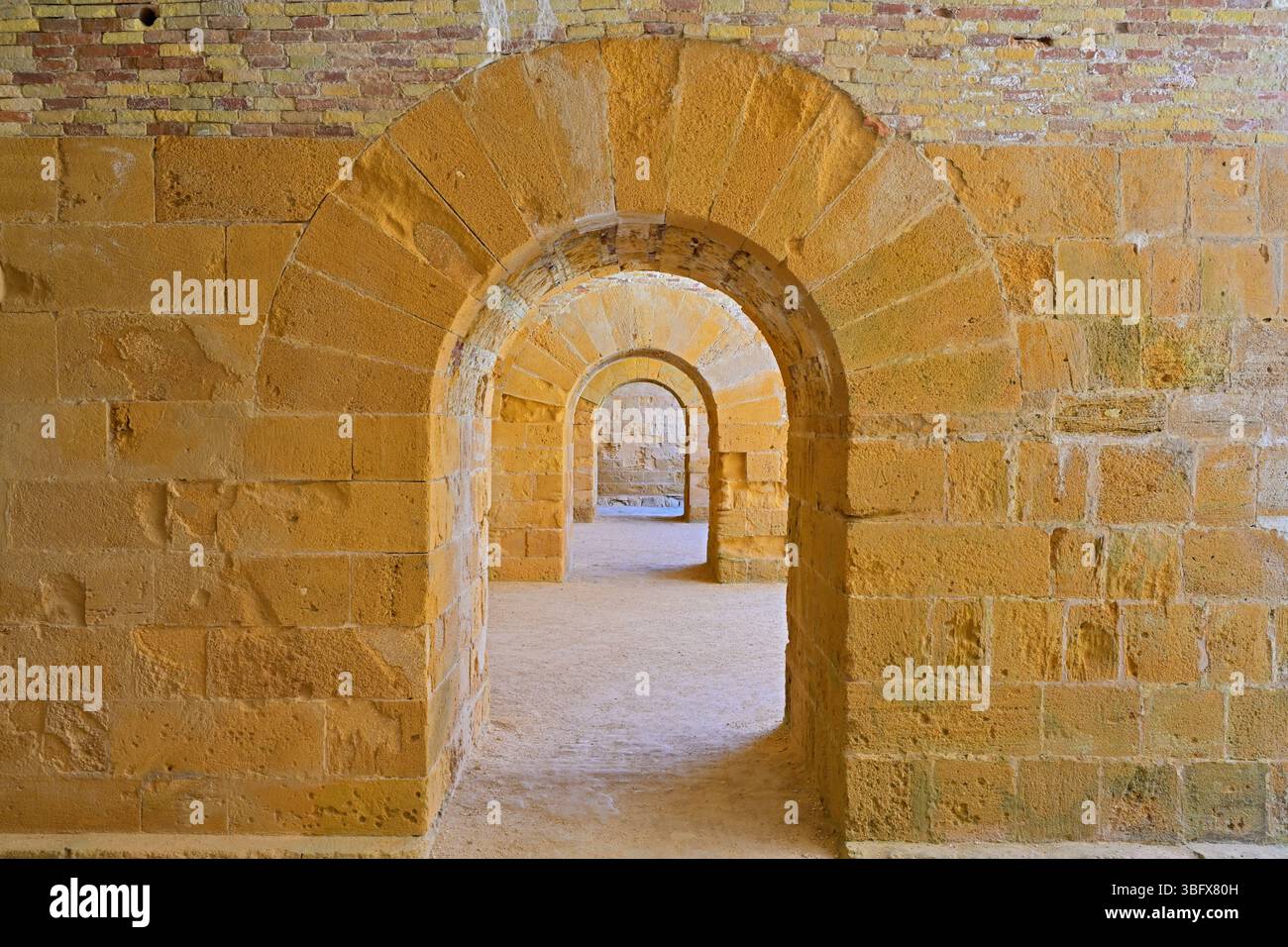 Sich wiederholende Steinbögen, die eine rückläufige Perspektive schaffen. Alte Steinbögen bilden einen linearen Durchgang in einem alten mittelalterlichen Gebäude. Stockfoto