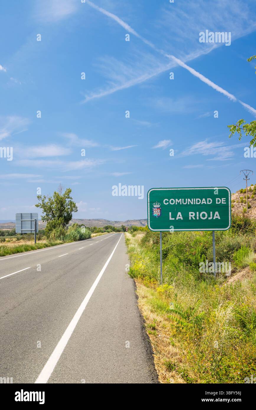 Leere Straße, die an einem sonnigen Sommertag mit Kondensstreifen am blauen Himmel in die Gemeinde La Rioja in Spanien führt Stockfoto