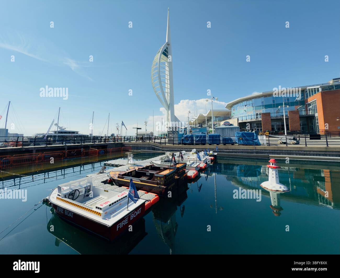 Portsmouth, England – 13. Mai 2025: Der Spinnaker Tower an den Gunwharf Quays erhebt sich an einem sonnigen Tag hinter den alten Docks. - Smartphone-aufgenommenes Stockfoto