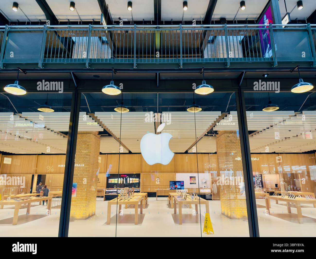 LONDON, GROSSBRITANNIEN – 23. MÄRZ 2025: Außenansicht des Apple Store in Battersea mit seiner ikonischen Glasfassade und dem beleuchteten Logo. - Smartphone-aufgenommenes Stockfoto