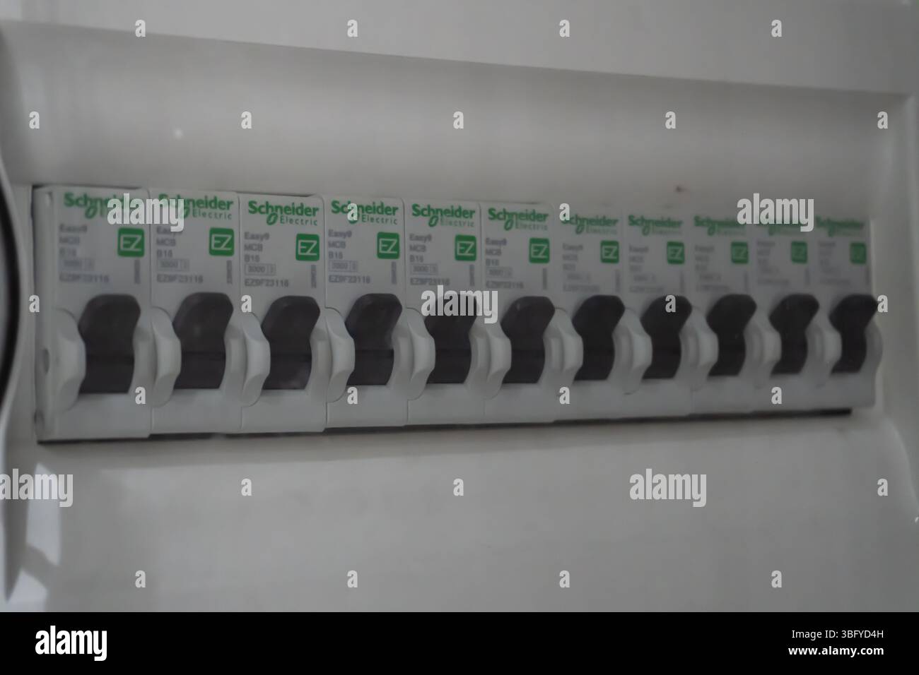 Nahaufnahme einer modernen elektrischen Verbrauchereinheit oder eines Sicherungskastens mit einer Reihe weißer Schneider-Leistungsschalter mit schwarzen Schaltern Stockfoto