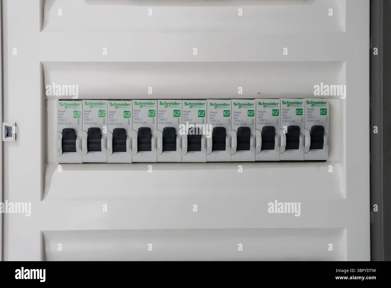 Nahaufnahme einer modernen elektrischen Verbrauchereinheit oder eines Sicherungskastens mit einer Reihe weißer Schneider-Leistungsschalter mit schwarzen Schaltern Stockfoto