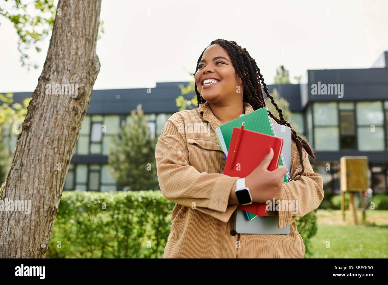 Ein Universitätslehrer lächelt herzlich und hält an einem sonnigen Campus-Tag lebhafte Notizbücher an. Stockfoto