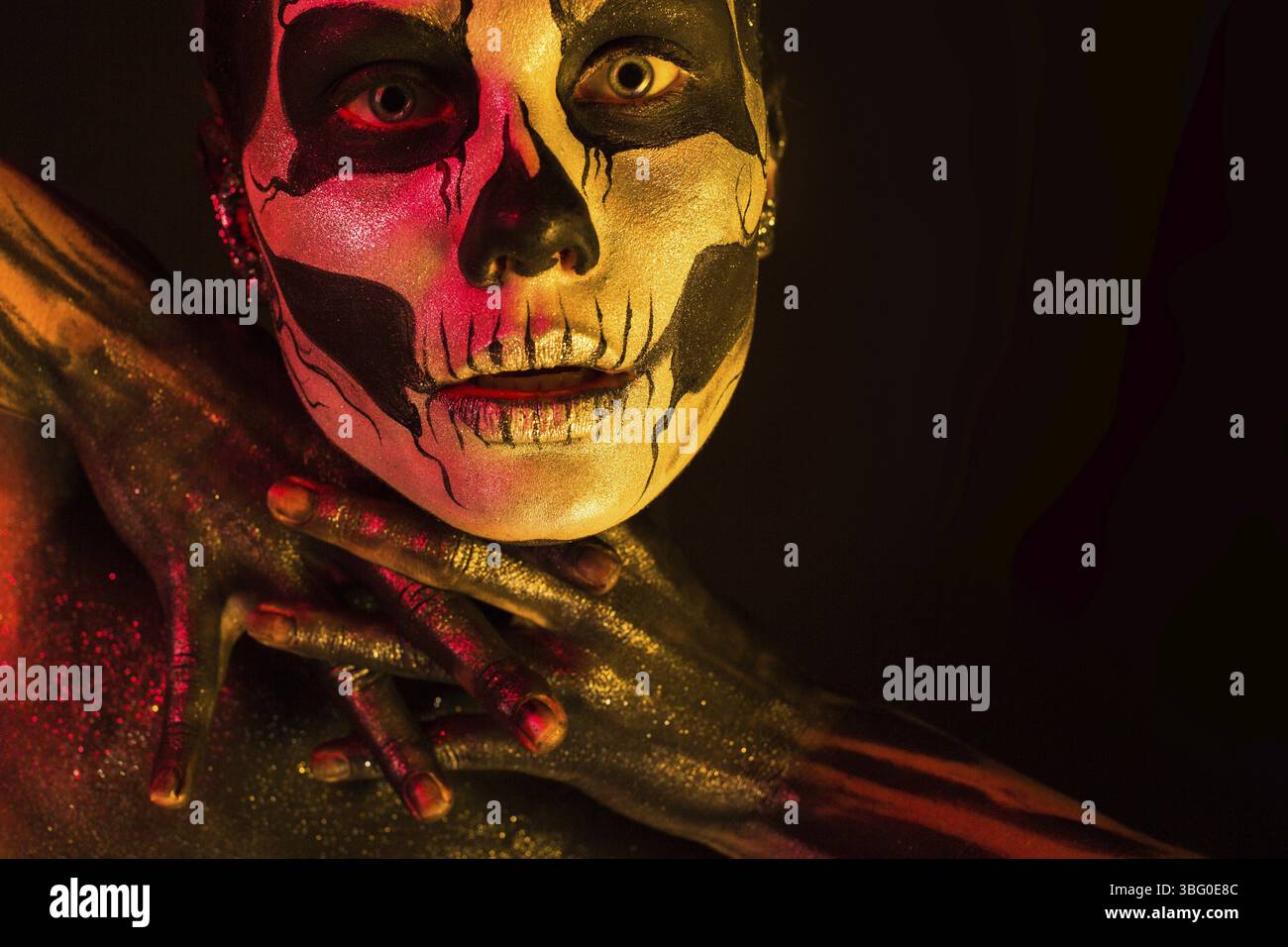 Isoliert auf Schwarz, Nahaufnahme, rot und gelb, schöne junge blonde weiße Frau mit Schädelkörperkunst, grauen Augen, gekreuzten Fingern Stockfoto